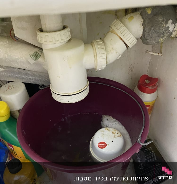 דליפה בצינור מתחת לכיור עם דלי מלא מים